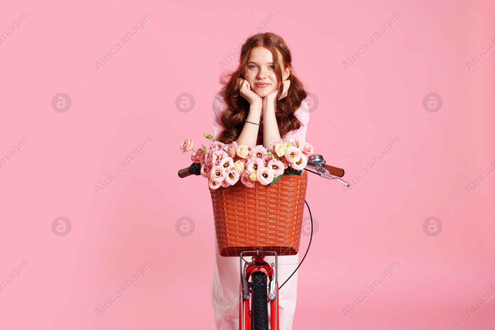 Beautiful teenage girl posing on bicycle with basket of flowers against pink background Photo of Beautiful teenage girl posing on bicycle with basket of flowers against pink background