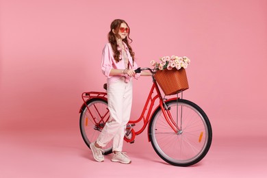Photo of Beautiful teenage girl in sunglasses and bicycle with basket of flowers against pink background