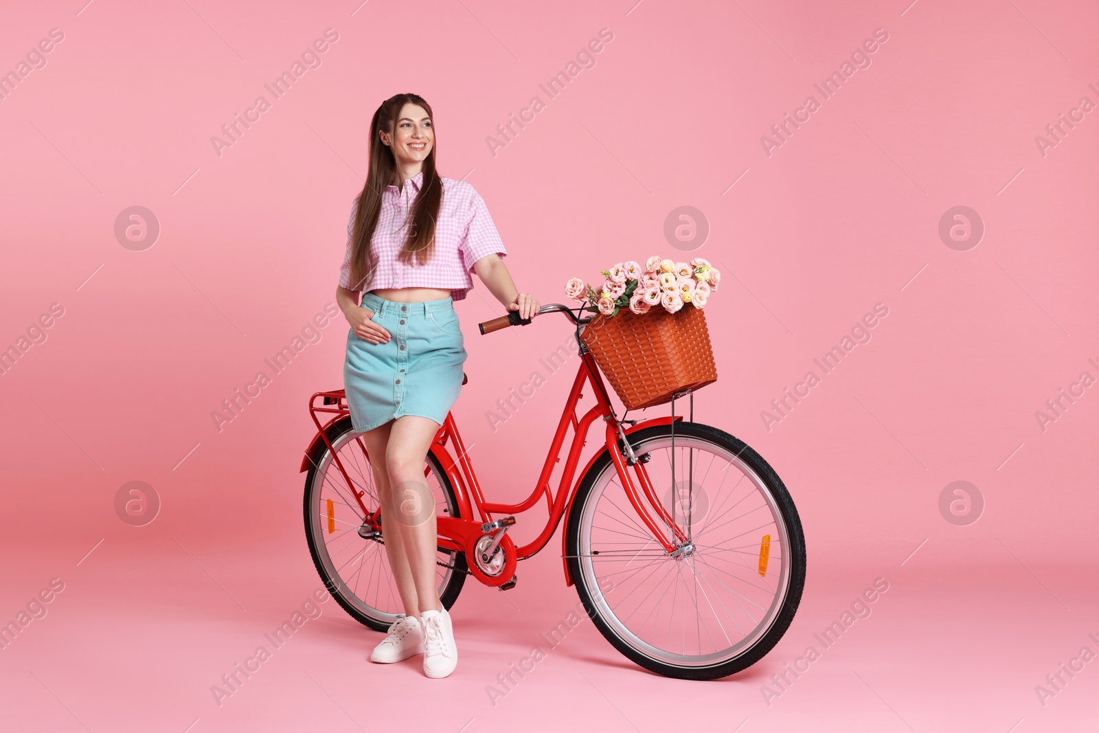 Photo of Smiling woman and bicycle with basket of flowers against pink background