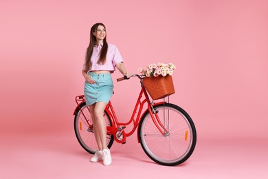 Photo of Smiling woman and bicycle with basket of flowers against pink background