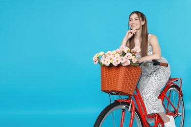 Photo of Smiling woman posing on bicycle with basket of flowers against light blue background. Space for text