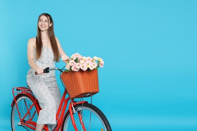 Photo of Smiling woman posing on bicycle with basket of flowers against light blue background. Space for text