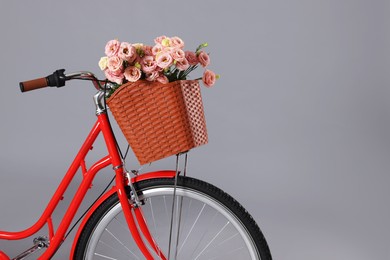 Photo of Bicycle with basket of beautiful flowers on grey background, closeup. Space for text