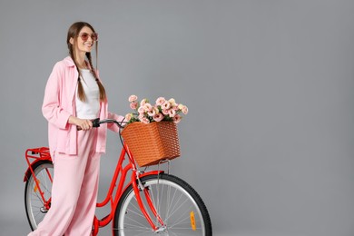Photo of Smiling woman in sunglasses and bicycle with basket of flowers against grey background. Space for text