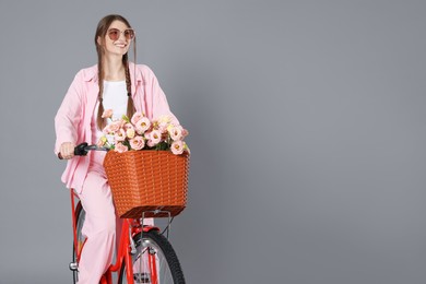 Photo of Smiling woman in sunglasses riding bicycle with basket of flowers against grey background. Space for text