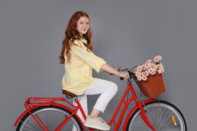 Photo of Beautiful teenage girl riding bicycle with basket of flowers against grey background
