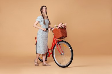 Photo of Smiling woman in dress and bicycle with basket of flowers on beige background