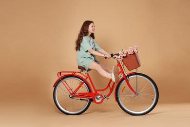 Photo of Smiling teenage girl riding bicycle with basket of flowers against beige background