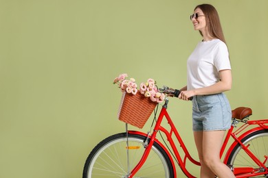 Photo of Smiling woman in sunglasses and bicycle with basket of flowers on green background. Space for text