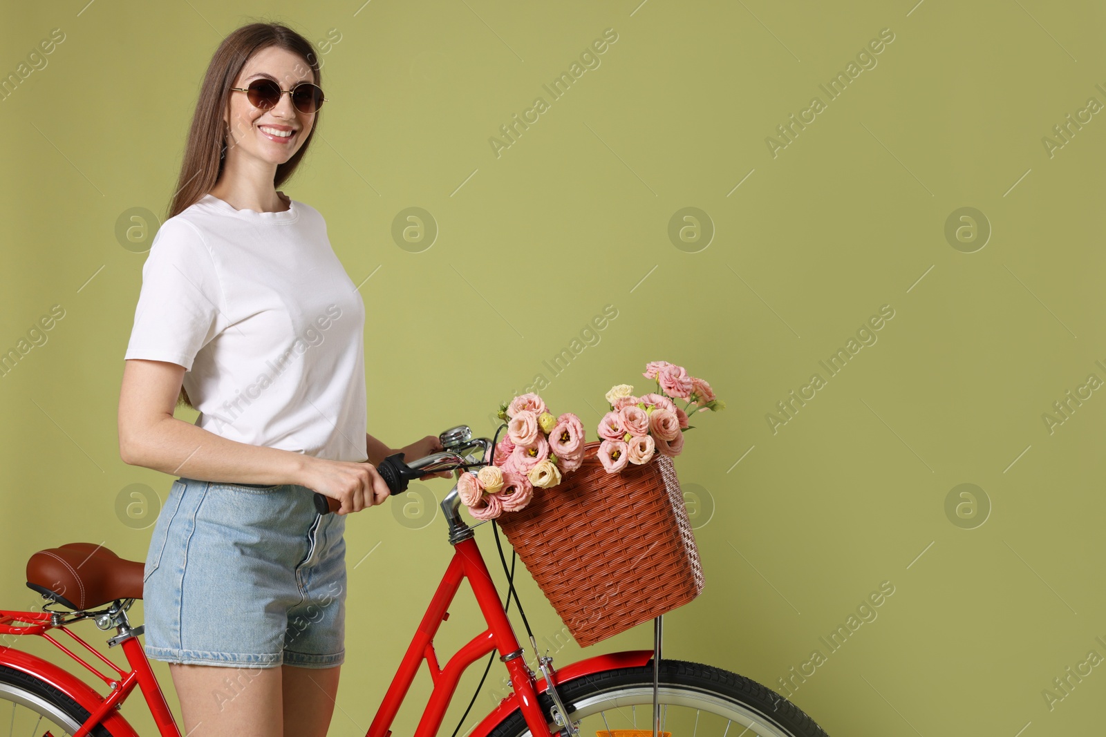 Photo of Smiling woman in sunglasses and bicycle with basket of flowers on green background. Space for text