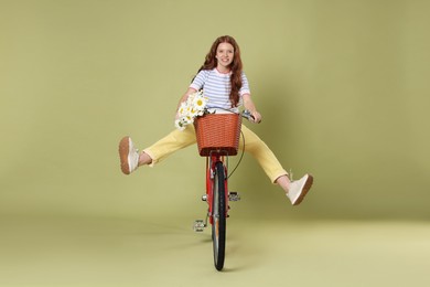 Photo of Smiling teenage girl riding bicycle with basket of flowers against green background