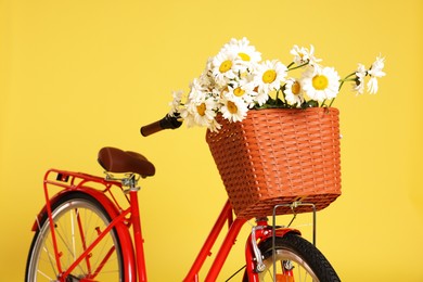 Photo of Bicycle with basket of beautiful flowers on yellow background, closeup