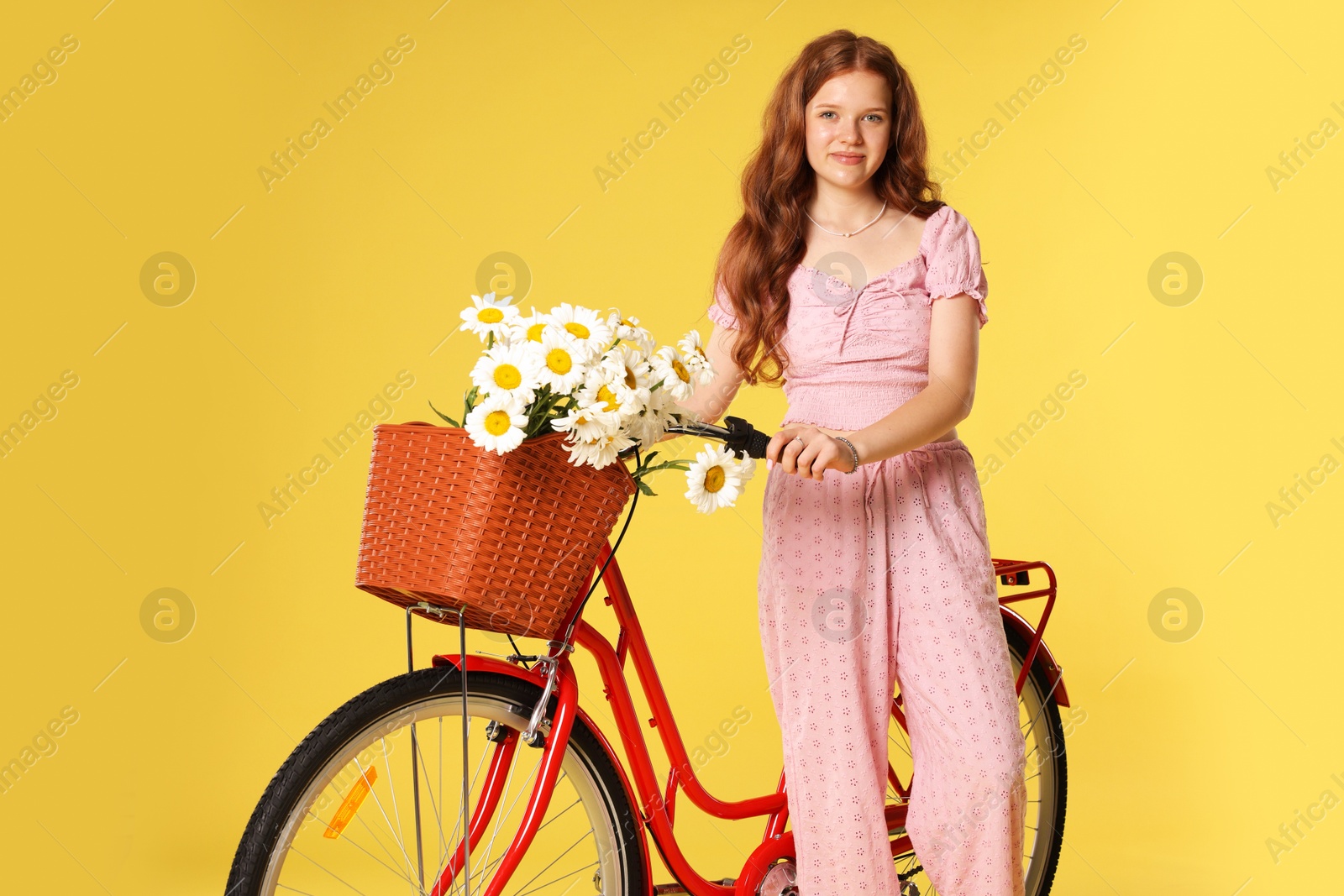 Beautiful teenage girl and bicycle with basket of flowers against yellow background Photo of Beautiful teenage girl and bicycle with basket of flowers against yellow background