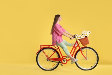 Photo of Smiling woman riding bicycle with basket of flowers against yellow background. Space for text