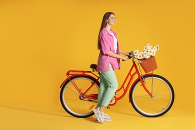 Photo of Smiling woman and bicycle with basket of flowers against yellow background. Space for text