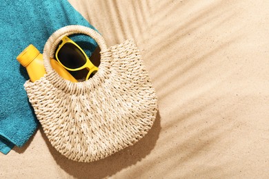 Photo of Beach towel, straw bag, sunscreen product and sunglasses on sand outdoors, flat lay. Space for text