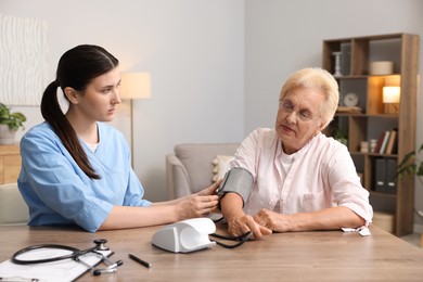 Photo of Nurse measuring patient's blood pressure at wooden table indoors. Home health care service