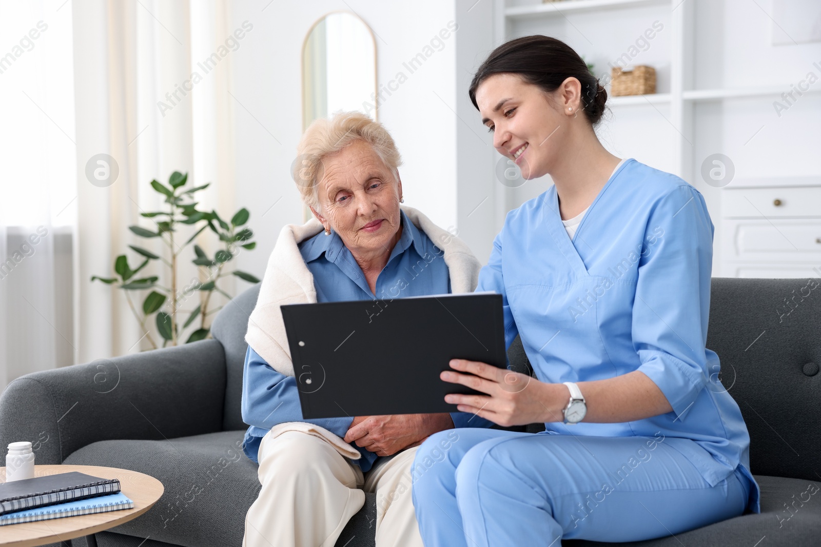 Photo of Nurse with clipboard examining senior woman indoors. Home health care service