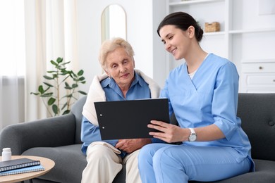 Photo of Nurse with clipboard examining senior woman indoors. Home health care service
