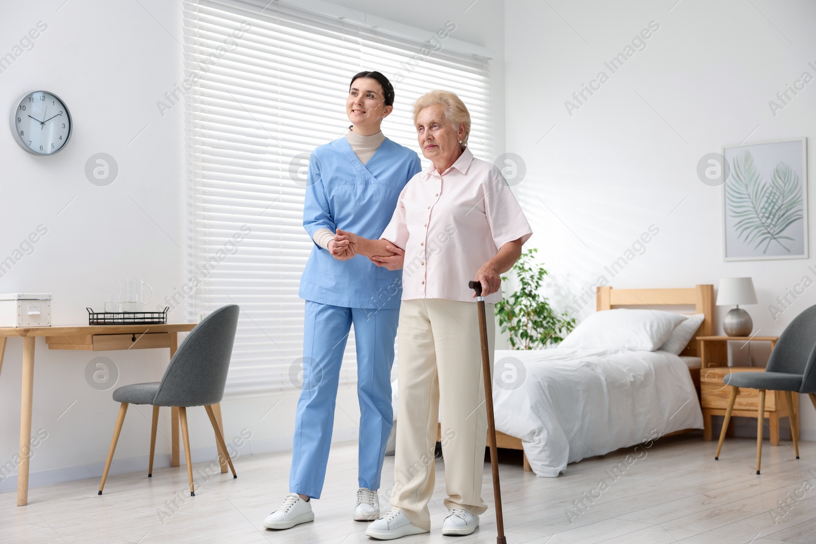 Nurse assisting senior woman with walking cane indoors. Home health care service Photo of Nurse assisting senior woman with walking cane indoors. Home health care service