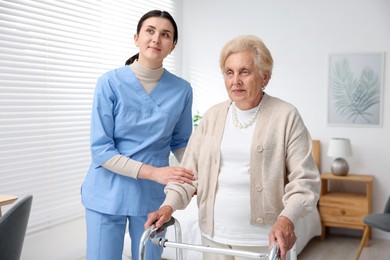 Photo of Nurse assisting senior woman with walking frame indoors. Home health care service