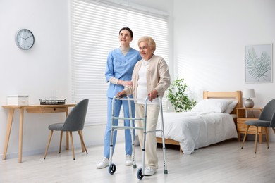 Photo of Nurse assisting senior woman with walking frame indoors. Home health care service