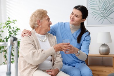 Photo of Nurse giving glass of water to senior woman indoors. Home health care service