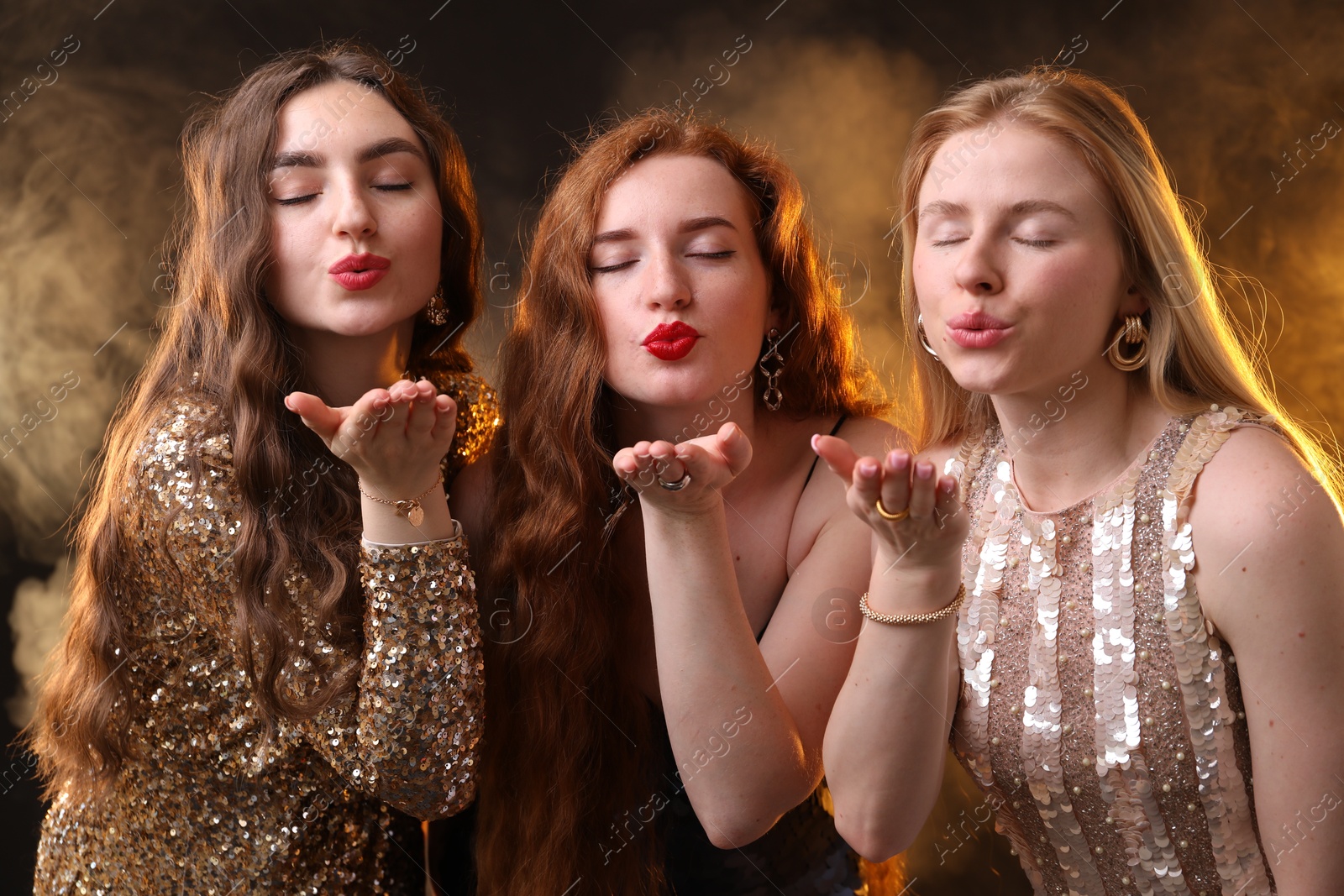 Beautiful women with different hair colors blowing kisses on dark background with smoke Photo of Beautiful women with different hair colors blowing kisses on dark background with smoke