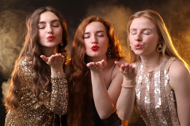 Photo of Beautiful women with different hair colors blowing kisses on dark background with smoke