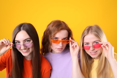 Photo of Beautiful women with different hair colors wearing stylish sunglasses on orange background