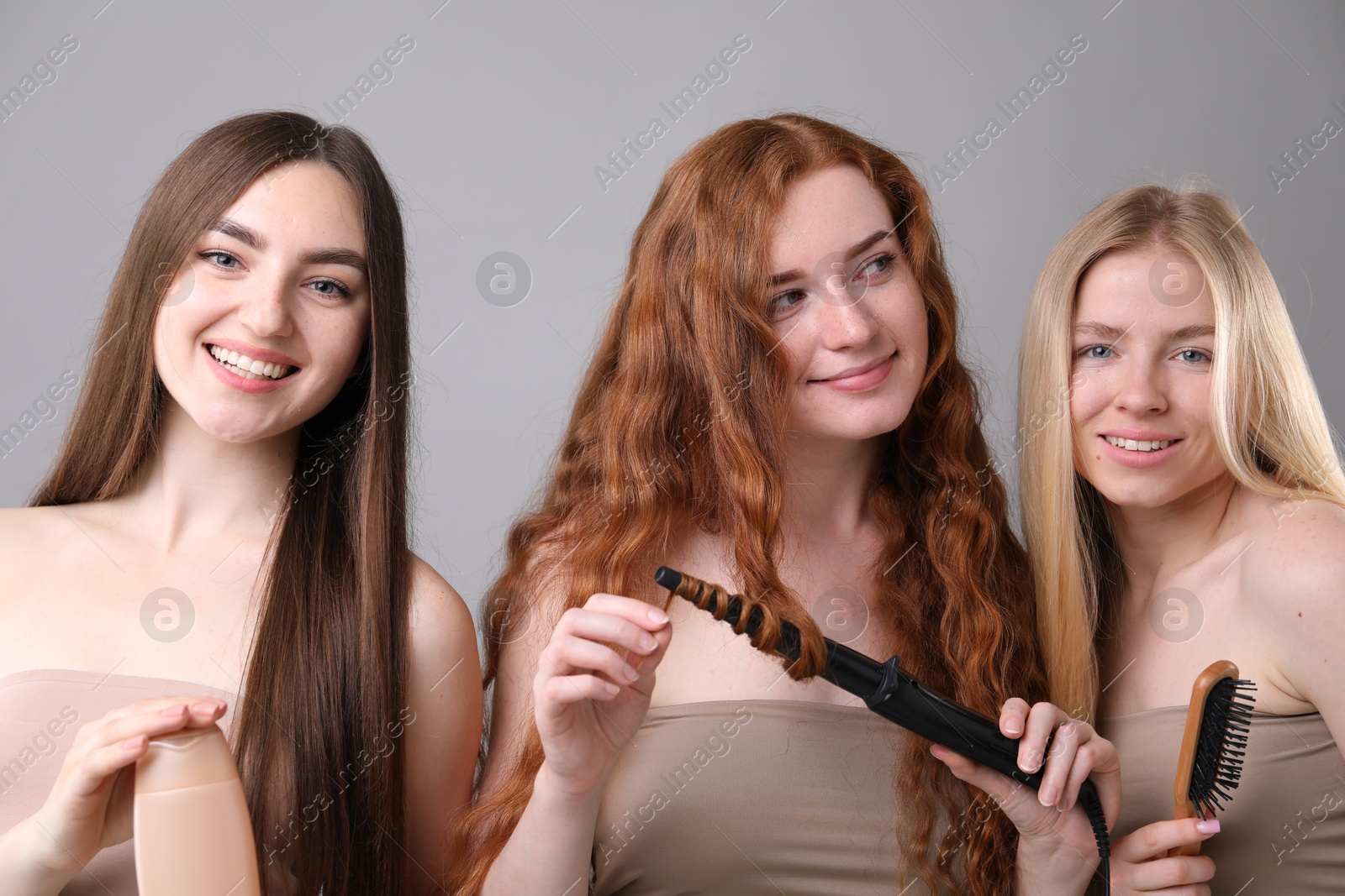 Beautiful women with different hair colors holding curling iron, shampoo and brush on grey background Photo of Beautiful women with different hair colors holding curling iron, shampoo and brush on grey background
