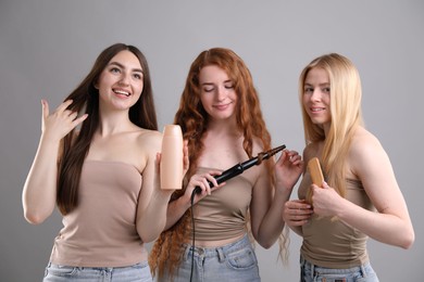 Photo of Beautiful women with different hair colors holding curling iron, shampoo and brush on grey background