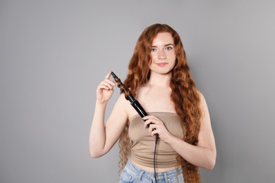 Photo of Beautiful woman with long wavy hair and curling iron on grey background, space for text