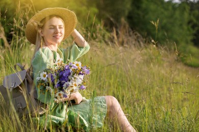 Photo of Woman with beautiful wildflowers, hat and backpack in meadow on sunny day. Space for text