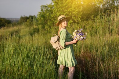 Photo of Woman with beautiful wildflowers, hat and backpack in meadow on sunny day