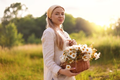 Photo of Happy woman with basket full of beautiful wildflowers outdoors