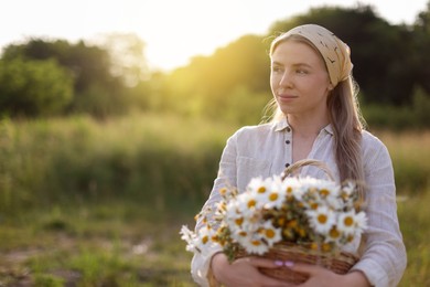 Photo of Happy woman with basket full of beautiful wildflowers outdoors