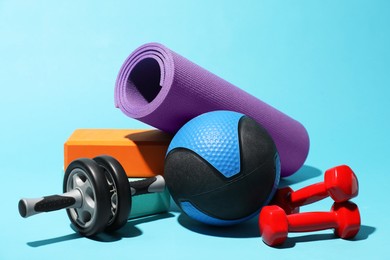Photo of Medicine ball, ab wheel, foam blocks, fitness mat and dumbbells on light blue background