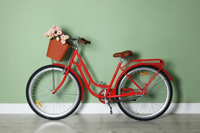 Photo of Bicycle with basket of beautiful flowers near light green wall indoors
