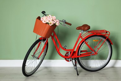Photo of Bicycle with basket of beautiful flowers near light green wall indoors