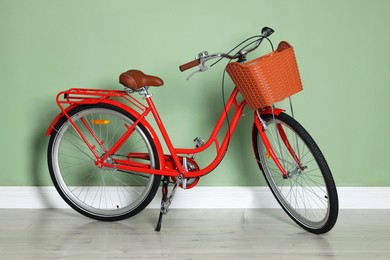 Photo of Red bicycle with basket near light green wall indoors