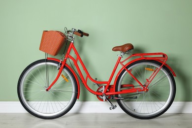 Photo of Red bicycle with basket near light green wall indoors