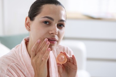 Photo of Young woman with lip balm at home, space for text