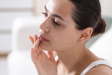 Photo of Young woman with lip balm on her lips at home