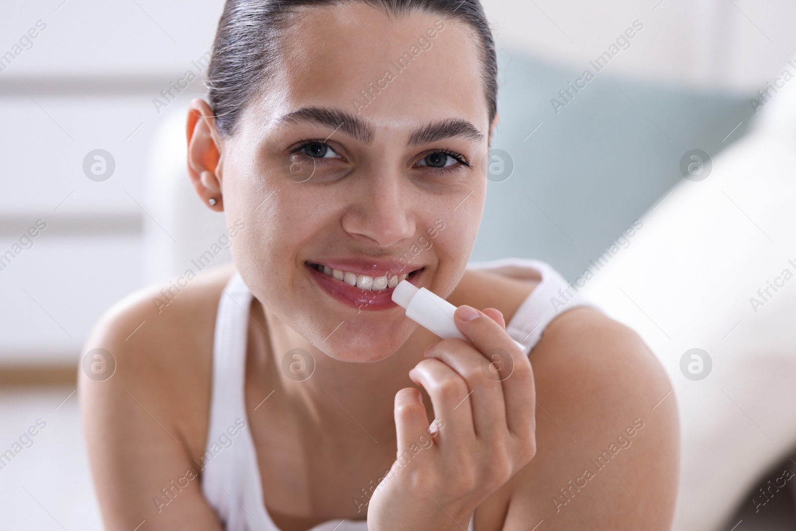 Young woman with lip balm at home Photo of Young woman with lip balm at home