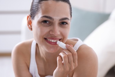Photo of Young woman with lip balm at home