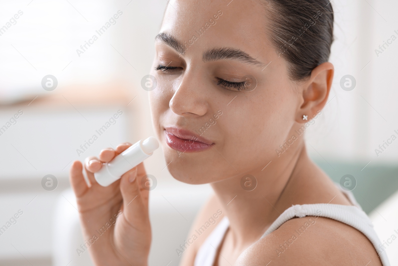 Photo of Young woman with lip balm at home