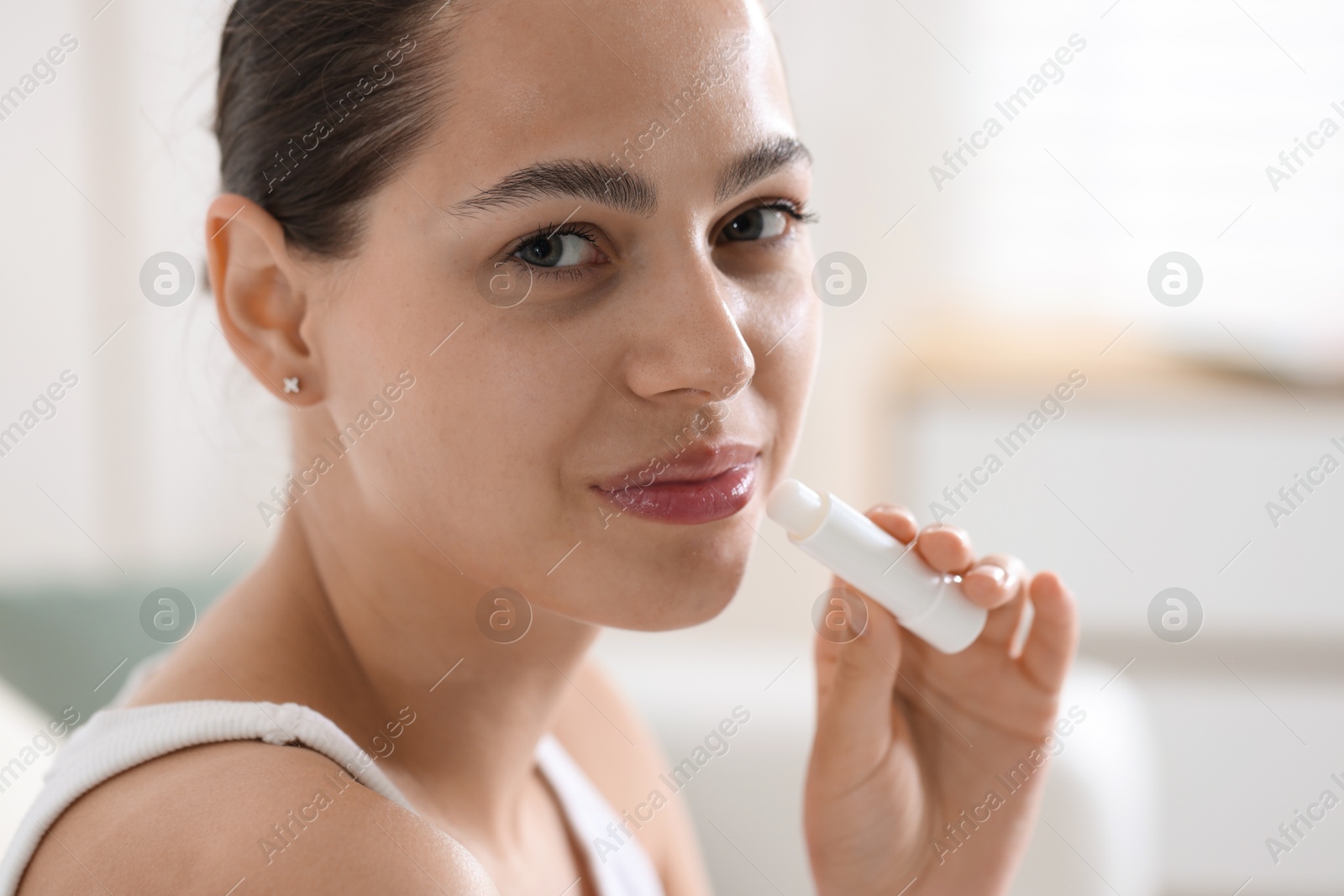 Young woman with lip balm at home Photo of Young woman with lip balm at home