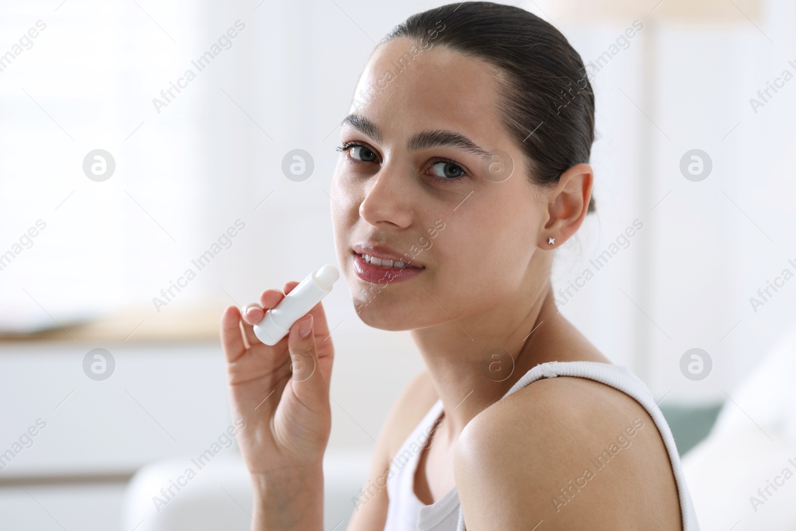 Young woman with lip balm at home Photo of Young woman with lip balm at home