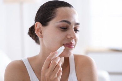 Photo of Young woman with lip balm at home